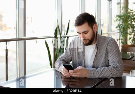 Phone conversation. Portrait smiling smart beard man in modern office with smartphone, texting messaging on application, check email, browsing Stock Photo