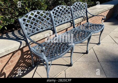 three 3 joined beautiful vintage old green metal garden chairs bench in the morning sunlight with shadows and shrubs Stock Photo