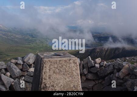 A view from the top of the Quinag mountain range, Scotland with the trig point, stone wind shelter, mountain tops and sky Stock Photo