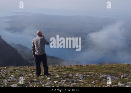 A view from the top of the Quinag mountain range, Scotland with 60+ man looking at the mountain tops, loch and sky Stock Photo