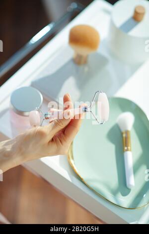 Closeup on woman holding calming quartz roller massager near table with toiletries at home in sunny winter day. Stock Photo