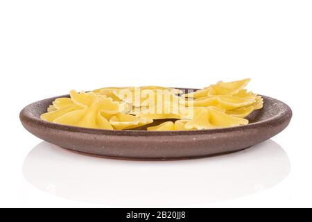 Lot of whole yellow pasta farfalle with brown ceramic coaster isolated on white background Stock Photo