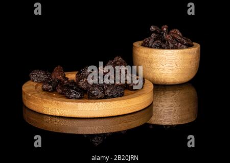 Lot of whole dried dark raisin in bamboo bowl on round bamboo coaster isolated on black glass Stock Photo
