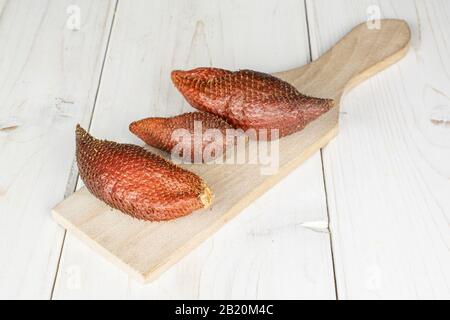 Group of three whole exotic brown salak on wooden cutting board on white wood Stock Photo