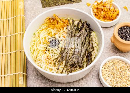 Noodles with seaweed, tuna flakes and sesame seeds. Healthy vegan (vegetarian) eating. In ceramic bowls, stone concrete background, close up
