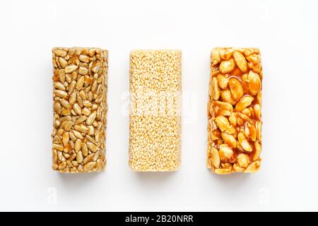 Grain granola bar with peanuts, sesame and seeds in a row on a white background. Top view Kozinaki Three assorted bars, isolate Stock Photo