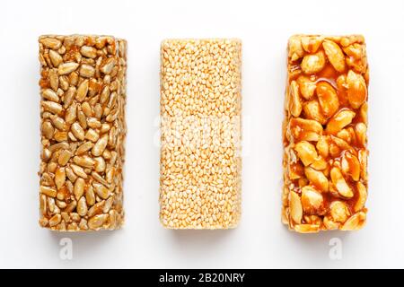 Grain granola bar with peanuts, sesame and seeds in a row on a white background. Top view Kozinaki Three assorted bars, isolate Stock Photo