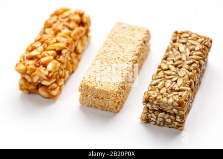 Grain granola bar with peanuts, sesame and seeds in a row on a white background. Top view Kozinaki Three assorted bars, isolate Stock Photo