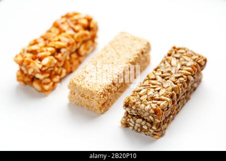 Grain granola bar with peanuts, sesame and seeds in a row on a white background. Top view Kozinaki Three assorted bars, isolate Stock Photo