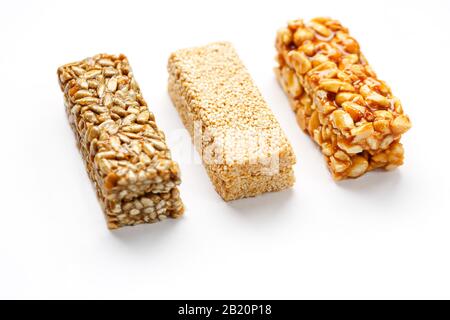 Grain granola bar with peanuts, sesame and seeds in a row on a white background. Top view Kozinaki Three assorted bars, isolate Stock Photo