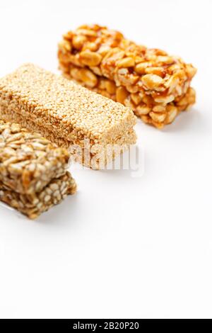 Grain granola bar with peanuts, sesame and seeds in a row on a white background. Top view Kozinaki Three assorted bars, isolate Stock Photo
