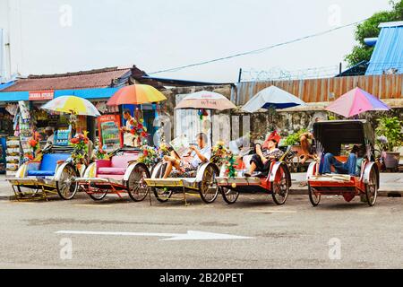 Georgetown, Penang, Malaysia - September 01, 2014: Vintage trishaw parking at street of George town. Group of rickshaw driver men rest and wait Stock Photo