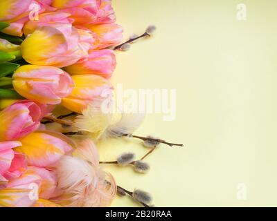 Easter decoration with pink tulips, willow branches, colorful eggs on yellow background. Greeting card for spring holidays, copy space Stock Photo