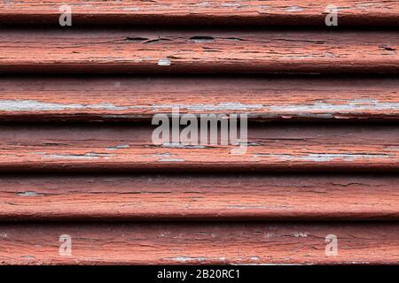 Close up of a dirty old red wooden window shutter with weathered and cracked paint peeling off Stock Photo