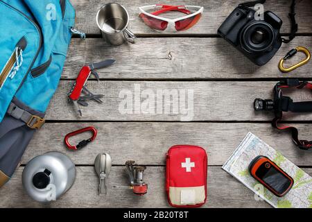 Top view of tourist equipment for travel and tourism on a rustic light wooden floor with an empty space in the middle. Items include a kettle, a card, Stock Photo