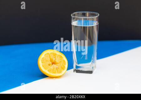 a glass of water stands next to a sliced lemon on a white-blue background Stock Photo