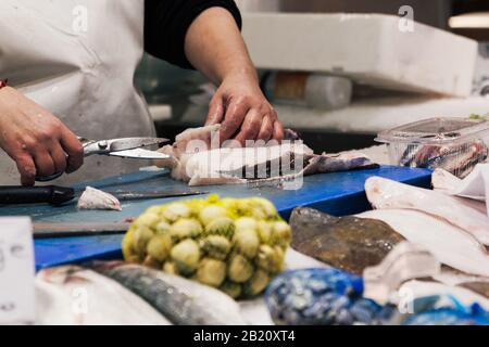 Stock photo of the hands of a fishmonger cutting a piece of fish with sharp scissors Stock Photo