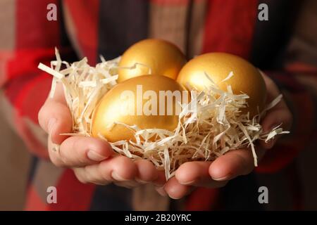 Woman in shirt holds nest with golden eggs, close up Stock Photo
