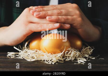 Female hands and nest with golden eggs on wooden table, close up Stock Photo