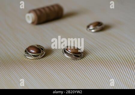 Three vintage buttons and a spool of thread. Elegant brown buttons on the table. Sewing and repair of clothes. Side view. Focus in the foreground. Eye Stock Photo
