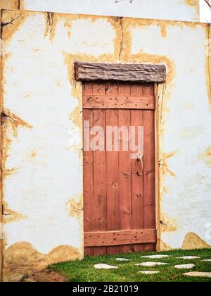 front view of wooden closed door on weathered wall with a grass bed Stock Photo