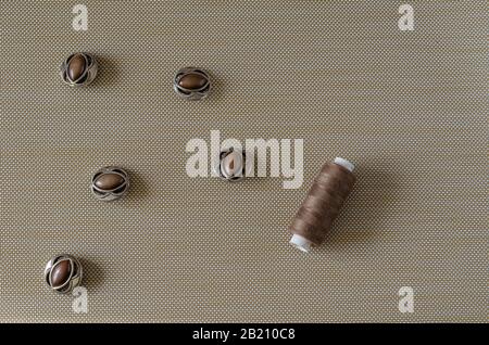 Brown buttons and threads background. Five buttons and spools of thread on a textured table. View from above. Selective focus. Conceptual background. Stock Photo