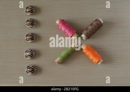 A line of buttons and spools of thread. Five brown buttons. Four multi-colored spools of thread. View from above. Selective focus. Conceptual backgrou Stock Photo