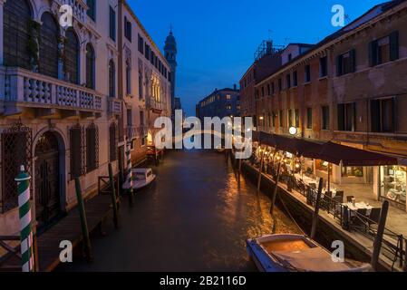 Evening atmosphere with restaurant on the canal, in the back the tower of the church Santa Maria della Pieta, Venice, Veneto. Italy Stock Photo