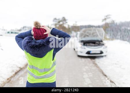 Frustrated female driver with hands on her head. Car breakdown road assistance concept. Winter scene. Stock Photo