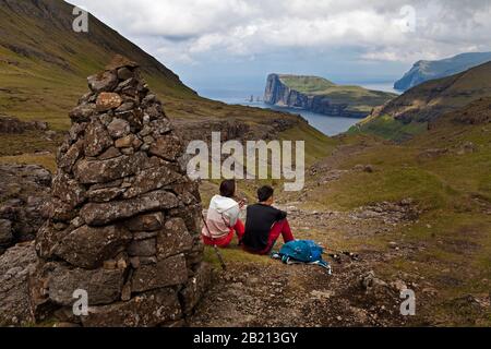 Two hikers taking a break with a view of the Atlantic Ocean, hiking trail from Tjornuvik to Saksun, Streymoy, Faroe Islands, Foroyar, Denmark Stock Photo