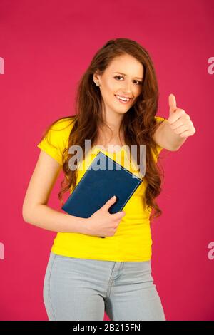 attractive young student in yellow t shirt holding red folder over pink background Stock Photo