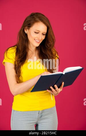 attractive young student in yellow t shirt holding red folder over pink background Stock Photo