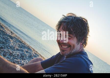 Handsome man relaxing on the beach in Greece while sunsets / Portrait of handsome middle aged man Stock Photo