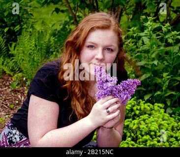 A pretty teen girl poses for a portrait with lilacs in a green garden, Stock Photo