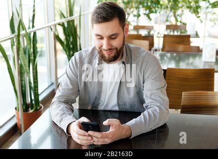 Phone conversation. Portrait smiling smart beard man in modern office with smartphone, texting messaging on application, check email, browsing Stock Photo