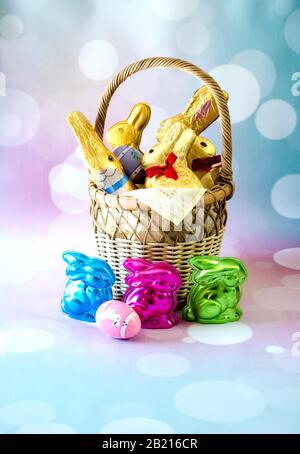 A decorative basket is filled with chocolate Easter bunnies and colored eggs Stock Photo