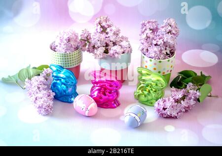 Colorful bunnies are filled with chocolate, and cups hold fragrant lilacs, in this pretty Easter still life Stock Photo