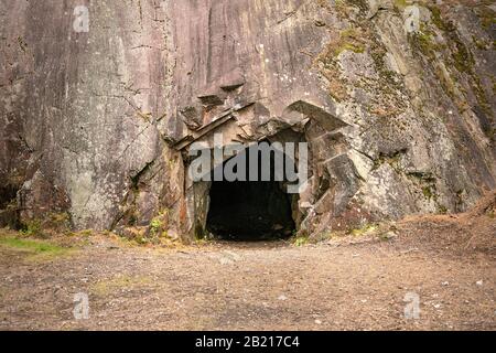 Rock wall with a dark hole, entrance to the cave in Spro, Mineral historic mine. Nesodden Norway. Nesoddtangen peninsula. Stock Photo