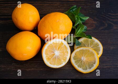 Meyer Lemons and Mint Sprigs on a Wood Background: A group of organic citrus fruits on a dark wooden cutting board Stock Photo