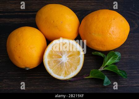 Meyer Lemons and Mint Sprigs on a Wood Background: A group of organic citrus fruits on a dark wooden cutting board Stock Photo
