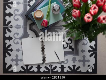 Overhead view of a pleasant scene with a still empty notebook with a pen over it and several horizontal books besides them and a beautiful bouquet of Stock Photo