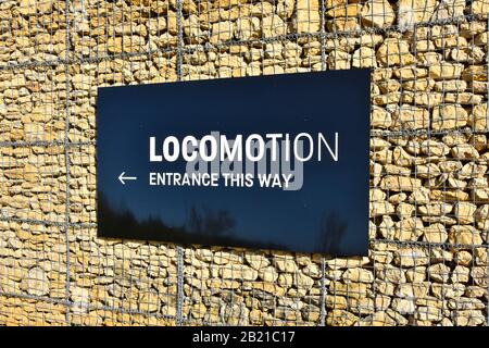 Sign for Locomotion  Museum entrance fixed on Gabion wire cage of broken quarry stone forming external battered building wall Shildon County Durham UK Stock Photo