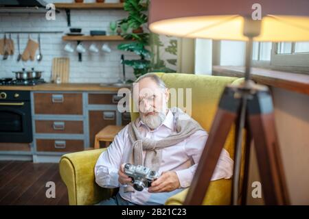Senior sitting in the armchair and holding a film camera Stock Photo