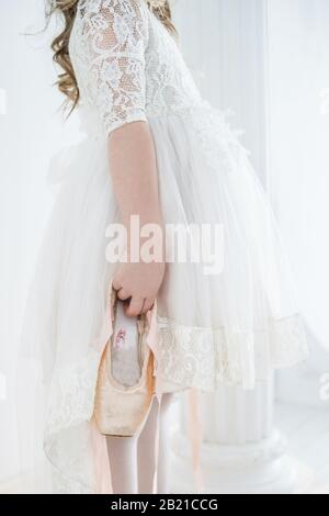 little girl ballerina in a beautiful white dress holding pointe shoes. Stock Photo