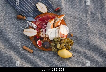 Top view of wooden board with pieces of bread pear figs nuts green grape and delicious cheese on blanket Stock Photo