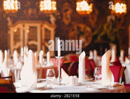 White candles in candlestick stylish glasses and folded napkins on plates in modern restaurant Stock Photo