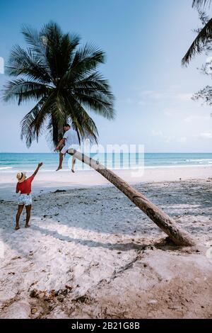 couple climbing in palm tree in Thailand, Wua Laen beach Chumphon area Thailand, palm tree hanging over the beach with couple on vacation in Thailand Stock Photo