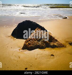 One white and one black stones in the yellow sand of sea shore. Wavy blue sea. Sunny day in Matalascanas, Spain Stock Photo