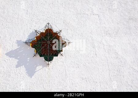 Multicolored stained glass window with patterned forged lattice on the white wall. Spanish style Stock Photo