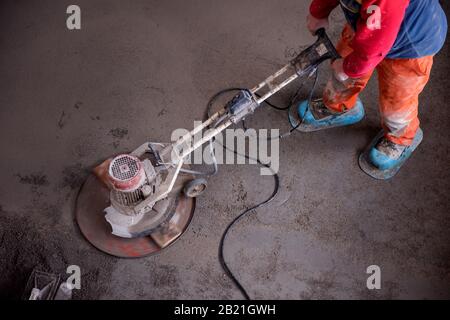 Laborer performing and polishing sand and cement screed floor on the construction site of a new two-level apartment. Sand and cement floor screed Stock Photo